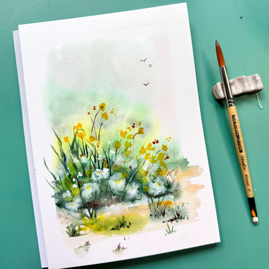 Loose yellow and green watercolor wildflower field beside a round brush on a teal table.